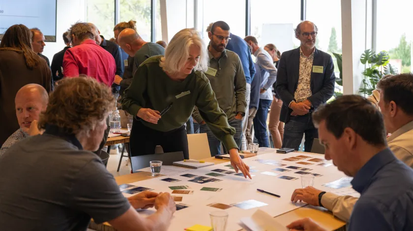 Deelnemers van de Impulsdag warmtenetten rond een tafel druk in de weer met kaarten uit de kaartenset ‘Crack the Process’