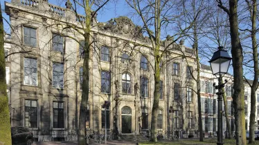 Stadspalies met bomen en oude lantaarnpaal ervoor. Voor de gevel staan fietsen.