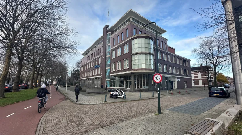 NPLW-gebouw met fietspad aan de linkerzijde, verder een fietser, lopend persoon en twee leenscooters op de voorgrond