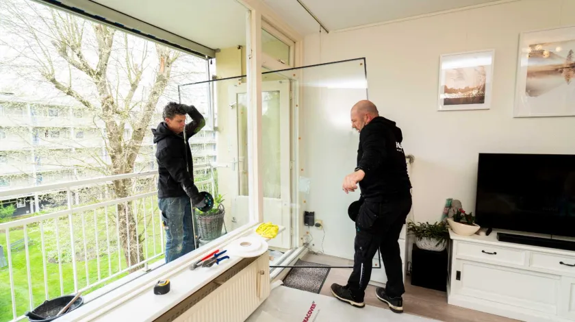 2 mannen lopen met een glazen raam door een woning in een flatgebouw.