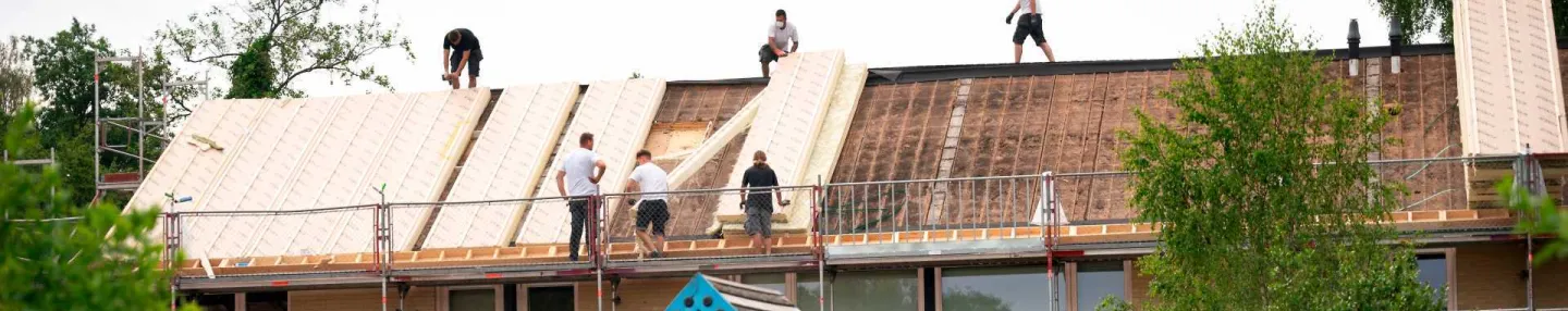 Foto van dakisolatiewerkzaamheden aan rijtjeshuizen met op de voorgrond een speelveldje met glijbaan