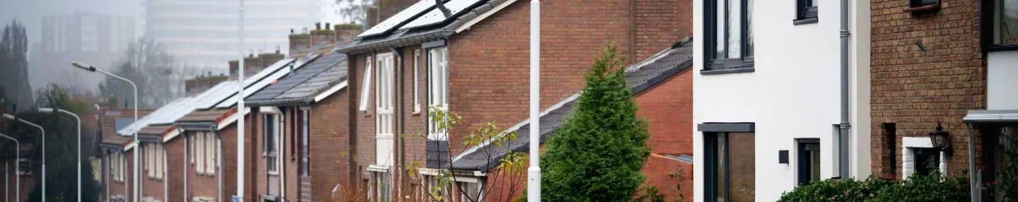 Straat met laagbouw met zonnepanelen op de schuine daken. In de verte 2 in nevelen gehulde flats