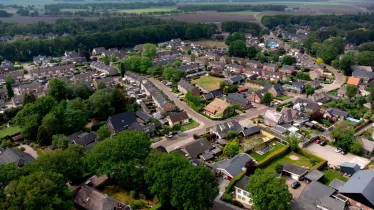 Dronebeeld van het dorp Dalen, gemeente Coevorden, met oude boerderijen en nieuwbouwwijken met op de achtergrond een coulisselandschap.