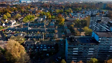 Luchtopname van hoog- en laagbouw met bomen in herfsttooi op de achtergrond in het Nijmeegse stadsdeel Dukenburg