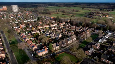 Luchtopname van laagbouw in de Wageningse wijk Benedenbuurt met in de verte links een hoge flat en rechts weilanden en bossen