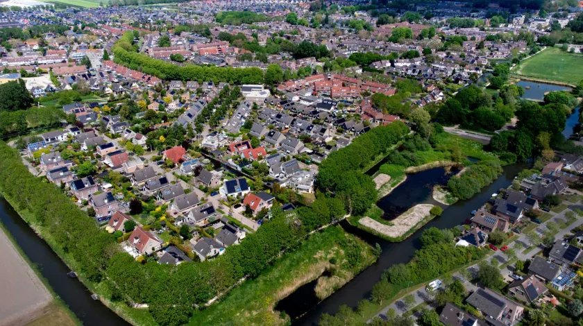 Luchtopname van eengezinswoningen in nieuwbouwwijken omringd door water en bomen in Gommerwijk-West, Enkhuizen met op de achtergrond het IJsselmeer.