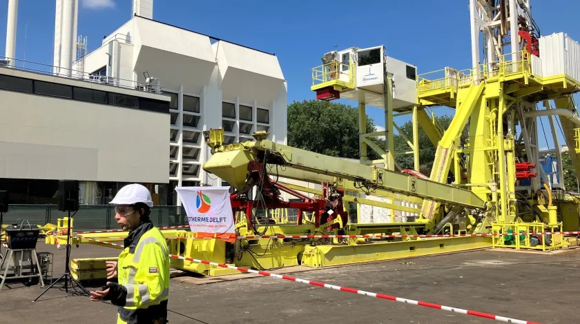 Bouwvakker met witte helm staat voor grote stalen constructie, onderdeel van de geothermie-installatie