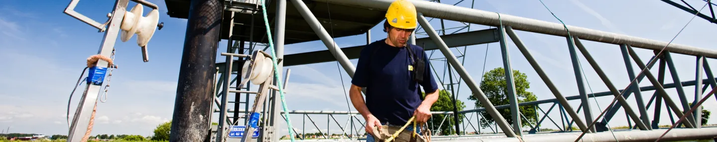 Monteur met gele helm staat op ponton waar een nieuwe elektriciteitsmast op ligt.