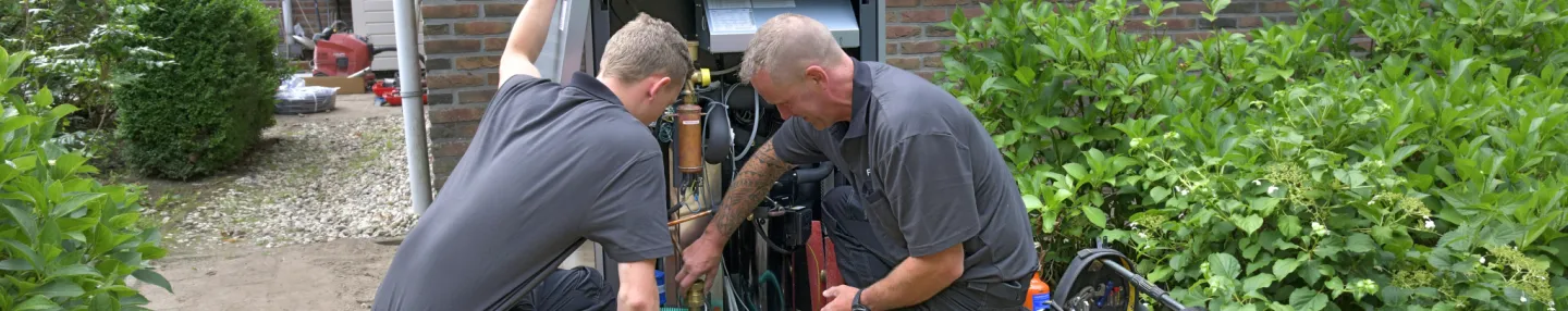 Twee monteurs zitten voor een huis en zijn bezig met de installatie van een warmtepomp